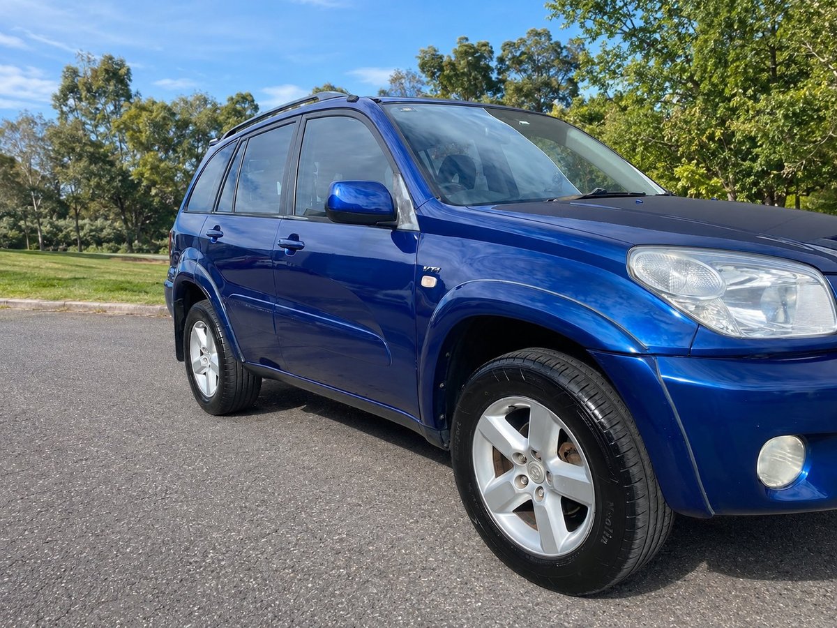 Blue compact SUV parked on asphalt with trees in background on sunny day
