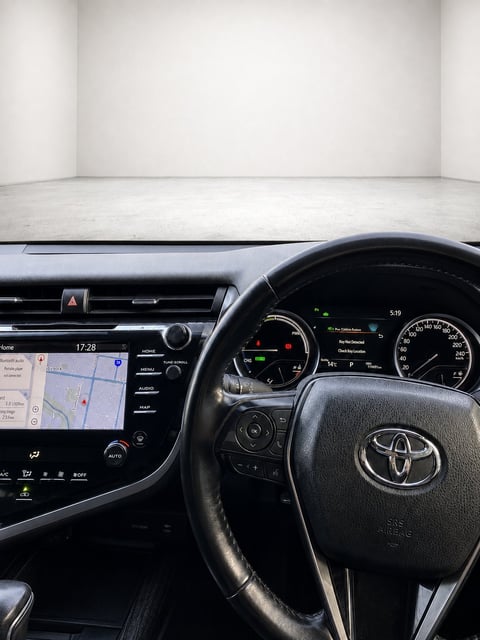 Toyota vehicle interior showing steering wheel, dashboard with navigation display, and gauges in a modern showroom setting
