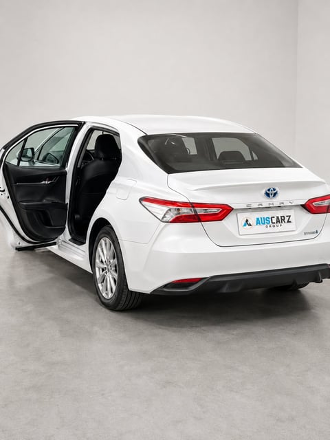 White Toyota Camry sedan with open driver-side door, displayed in a showroom against a light gray background