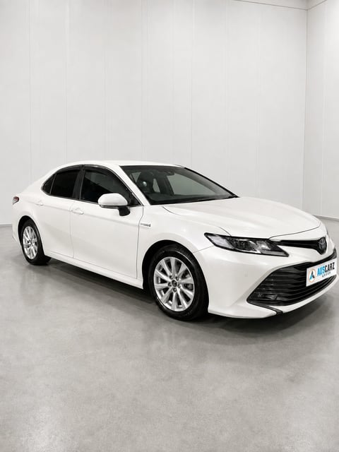 White Toyota Camry sedan displayed in a showroom with white walls and gray floor