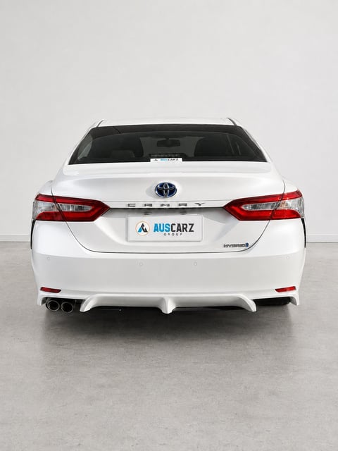 Rear view of a white Toyota Camry sedan with red taillights and AUSCARZ license plate on concrete background