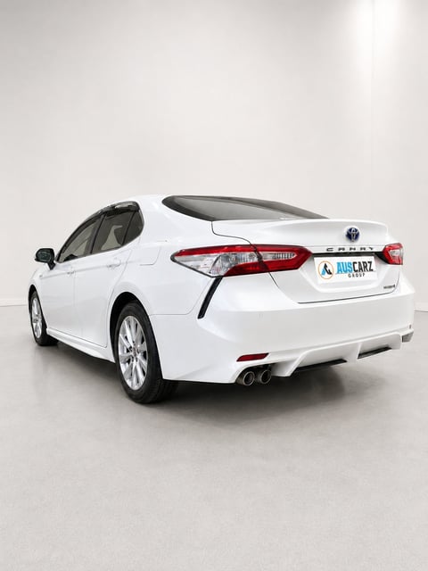 White Toyota Camry sedan with driver door open, shown from rear three-quarter angle in studio setting