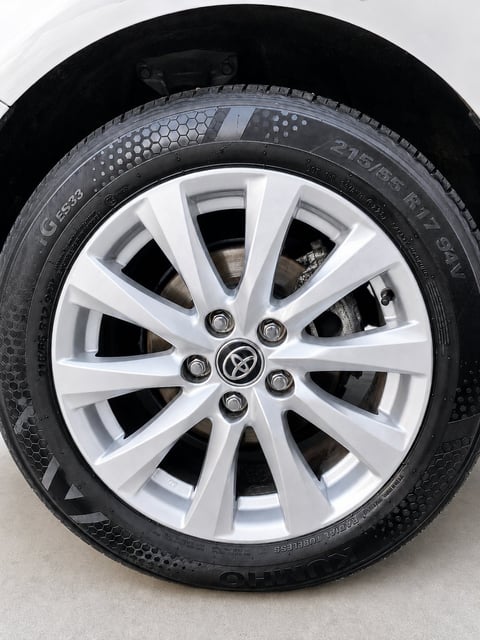 White alloy wheel with Toyota logo on vehicle tire, mounted on black rubber with hexagonal tread pattern